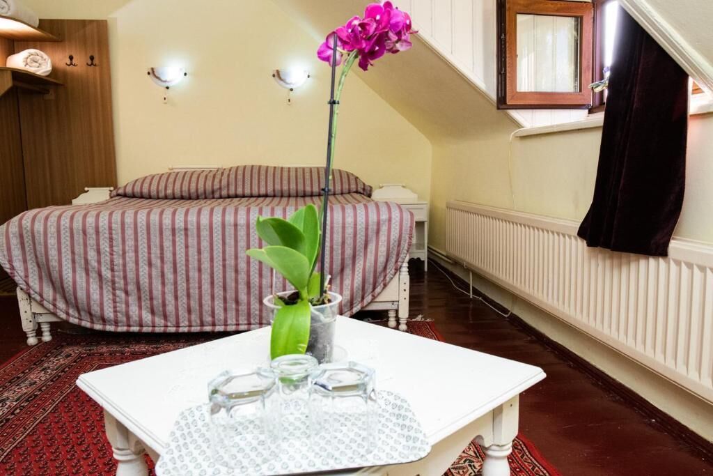 Um quarto com uma cama, uma mesinha com um vaso de flores e um radiador.