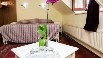 Um quarto com uma cama, uma mesinha com um vaso de flores e um radiador.