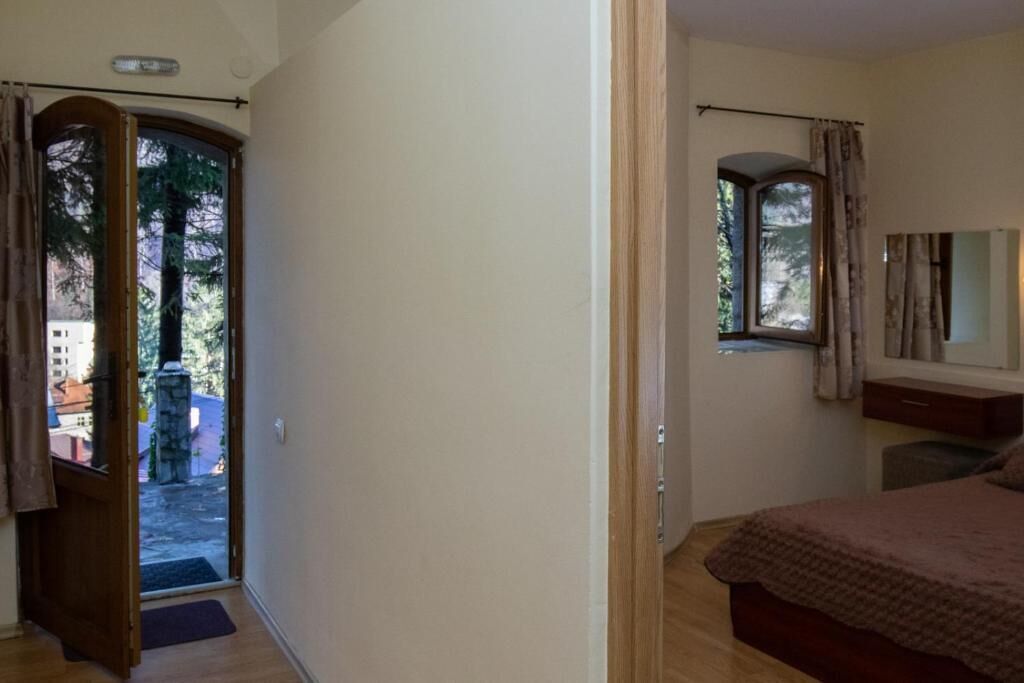 A bedroom with a bed, a window with curtains, a door leading outside, and a small table with chairs.