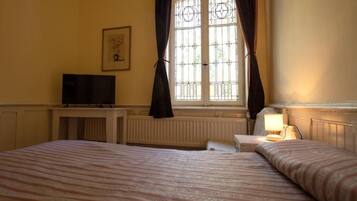 A hotel room with a bed, a bedside table with a lamp, a television, and a window with curtains.
