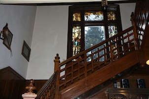 A wooden staircase with a balustrade leading to a room with a large stained glass window.