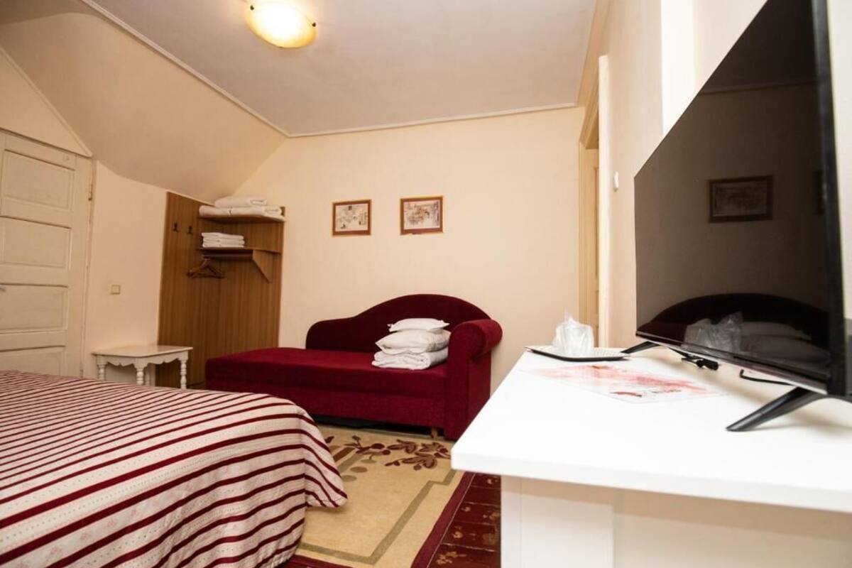 A hotel room with a bed, a red sofa, a desk with a computer, and a television.