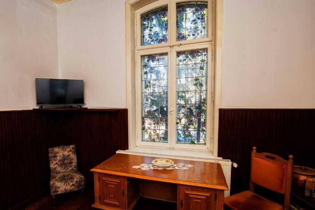 Una habitación con un escritorio de madera, una silla, un televisor y un ventanal con vidrieras.