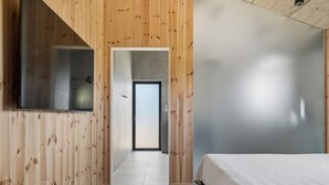 Ein modernes Schlafzimmer mit Holzvertäfelung, einem großen Bett und Blick in einen weiteren Raum.