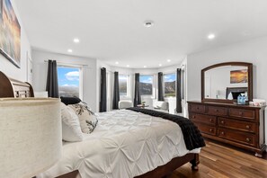 A bedroom with a bed, a dresser, a mirror, and a window with a view.