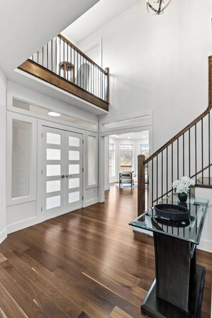 A spacious hallway with a wooden floor, a glass table with a basket, and a staircase with a railing.