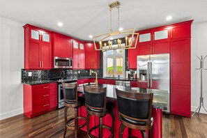 A modern kitchen with red cabinets, a black countertop, stainless steel appliances, and a bar area with stools.