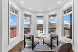 A corner room with large windows, two chairs, a small table, and a view of a hilly landscape.
