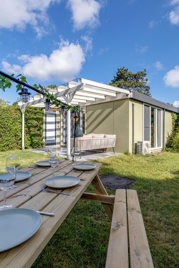 A wooden picnic table set outdoors with plates, cutlery, and glasses. - Bungalow with large private garden and BBQ place near Lake Veere (Kortgene)