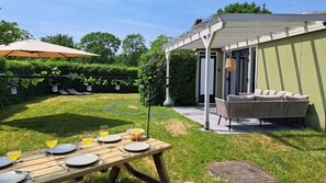 A patio with a table set for dining, a covered seating area, and a garden with a pergola. - Bungalow with large private garden and BBQ place near Lake Veere (Kortgene)