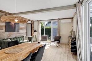 A dining area with a wooden table, chairs, and a woven pendant light. - Bungalow with large private garden and BBQ place near Lake Veere (Kortgene)