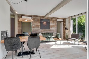Uma sala de estar moderna com uma parede de destaque em madeira, uma área de jantar com mesa e cadeiras de madeira, e uma janela grande que proporciona luz natural.