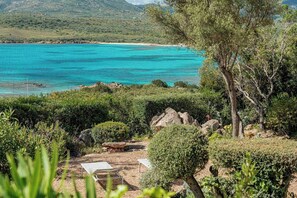 Eine Küstenlandschaft mit freiem Blick auf das Meer, einem Sandstrand und einem Gartenbereich mit Tisch und Stühlen.