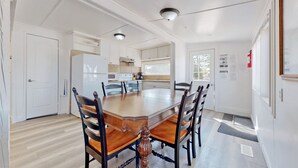 A dining area with a wooden table and chairs, a kitchen in the background, and a white door. - Beach 1 Getaway, Walk to Beach 1, Sleeps 10, Pet-Friendly, Fire Pit 93 Mosley St (Wasaga Beach)
