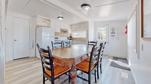 Un coin repas avec une table et des chaises en bois, une cuisine en arrière-plan et une porte blanche.