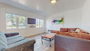 A living room with two sofas, a coffee table, a TV, and a painting on the wall. - Beach 1 Getaway, Walk to Beach 1, Sleeps 10, Pet-Friendly, Fire Pit 93 Mosley St (Wasaga Beach)