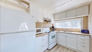 A compact kitchen with white cabinetry, a microwave, stove, and a sink. - Beach 1 Getaway, Walk to Beach 1, Sleeps 10, Pet-Friendly, Fire Pit 93 Mosley St (Wasaga Beach)