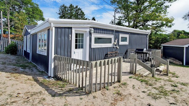 A small, single-story cabin with a front door, a window, and a small porch area. - Beach 1 Getaway, Walk to Beach 1, Sleeps 10, Pet-Friendly, Fire Pit 93 Mosley St (Wasaga Beach)