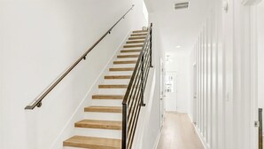 Una escalera con escalones de madera y barandillas metálicas, que conduce a un pasillo con paredes blancas y suelo de color claro.