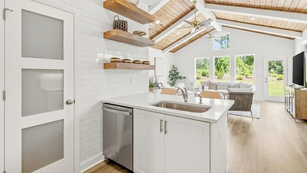 Una cocina moderna con armarios blancos, lavavajillas y vigas de madera en el techo.