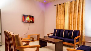 A living room with a sofa, two wooden chairs, a coffee table, and a television displaying a fire. - Imuhira Villa Kibenga – Peaceful 3-Bedroom Villa in Bujumbura (Bujumbura)