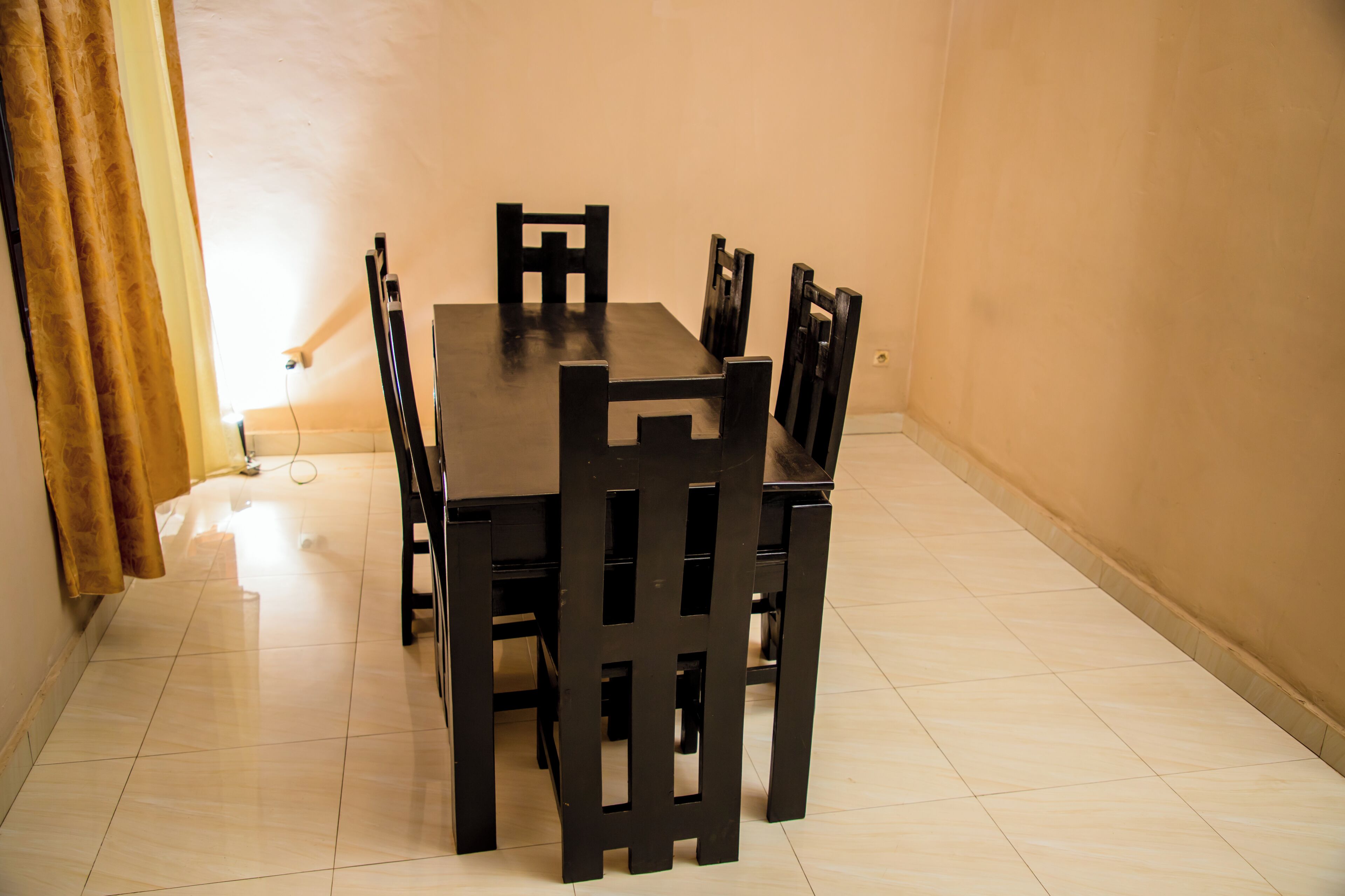 A dining area with a table and chairs, a curtain, and a light fixture on the wall.