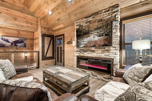 A log cabin interior with a stone fireplace, leather furniture, and a mounted TV. - New Cabin -Dollywood -Smokies -Great View! -Game Rm -PS4-Gatlinburg-Pigeon Forge (Sevierville)