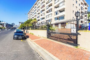 A multi-story building with a gated entrance, a paved sidewalk, and a parked car. - Chic Retreat in Green Point by Ctha (Cape Town)
