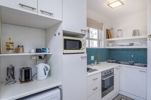 A modern kitchen with white cabinets, a microwave, a kettle, and a stove. - Chic Retreat in Green Point by Ctha (Cape Town)