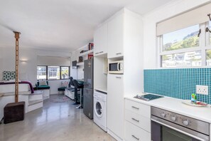 A compact kitchen with a washing machine, microwave, and stove. - Chic Retreat in Green Point by Ctha (Cape Town)