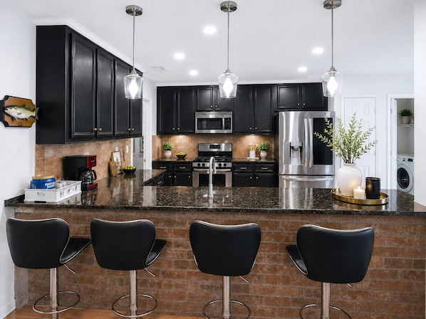 Una cocina moderna con armarios oscuros, electrodomésticos de acero inoxidable y una isla central con taburetes de bar.