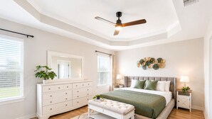 Une chambre à coucher comprenant un lit, une commode, un banc, un ventilateur de plafond et un élément décoratif mural.