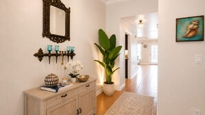 Un couloir avec une console en bois, un miroir, des appliques murales turquoise, une plante en pot et un tapis.