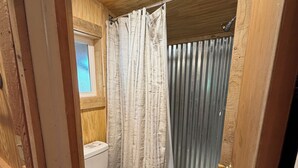 Et badeværelse med træpaneler, toilet, brusebad og et vindue.