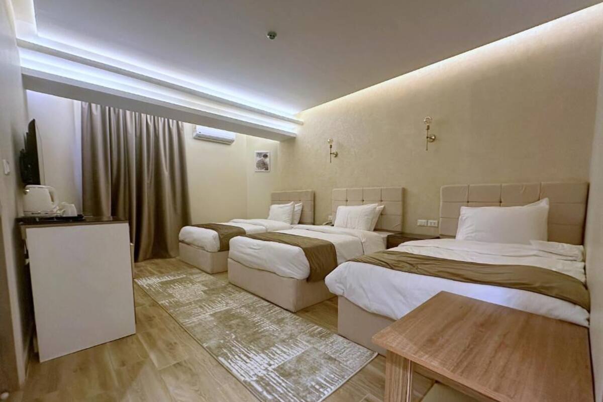 A hotel room with two beds, a small table, a desk, a coffee machine, and a window with curtains.