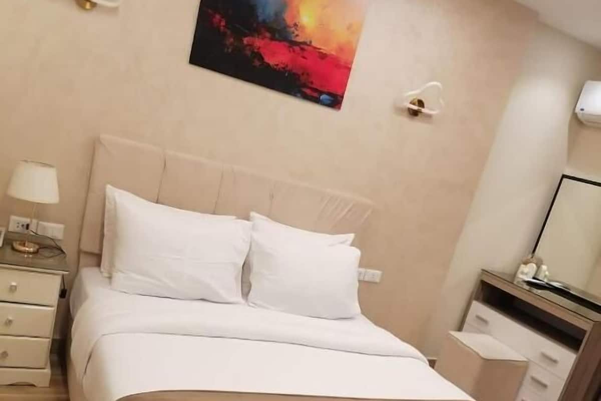 A neatly arranged hotel room with a bed, bedside tables, a nightstand, a mirror, and a painting on the wall.