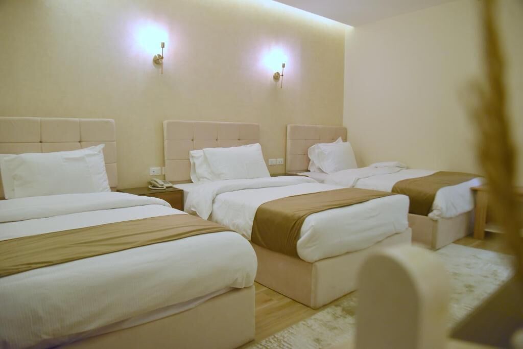A hotel room with three beds, a bedside telephone, and wall-mounted lights.