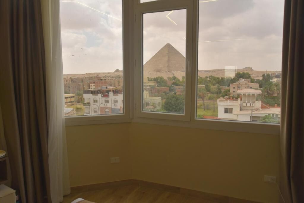 Een kamer met een groot raam, met uitzicht op een piramide en een stadsbeeld.