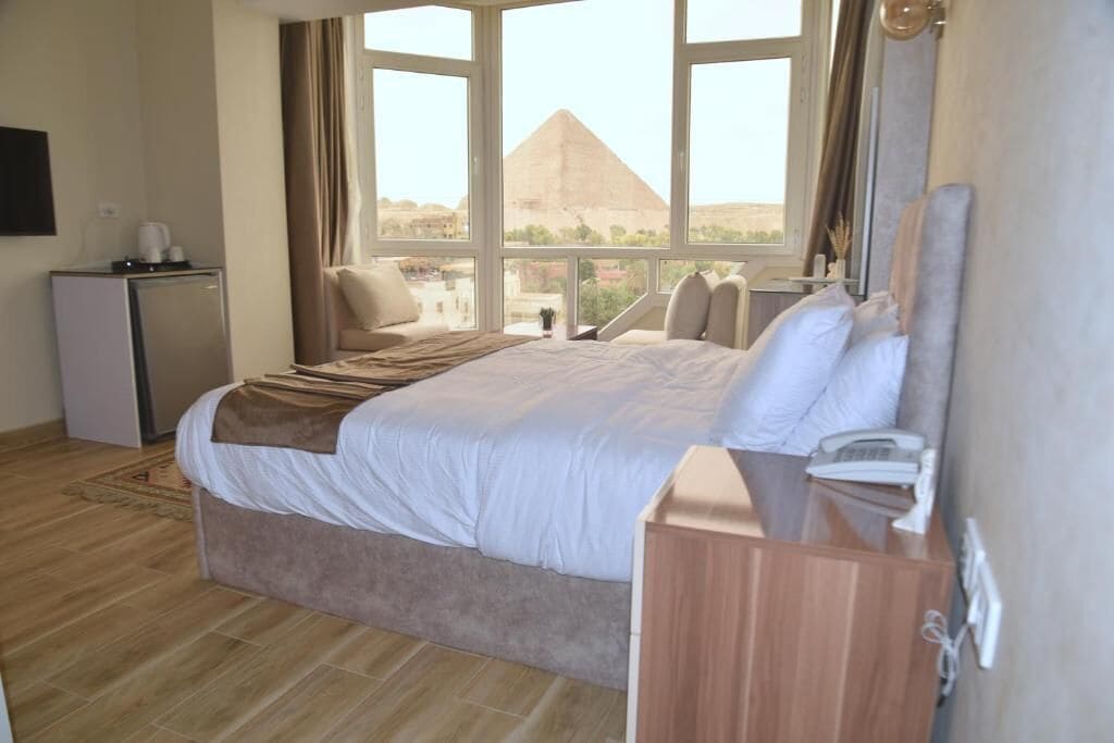 Een hotelkamer met een bed, een bureau, een telefoon en uitzicht op een piramide.