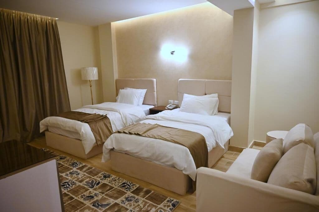 Hotellihuone, jossa on kaksi sänkyä, sohva, lamppu ja kuviollinen matto.