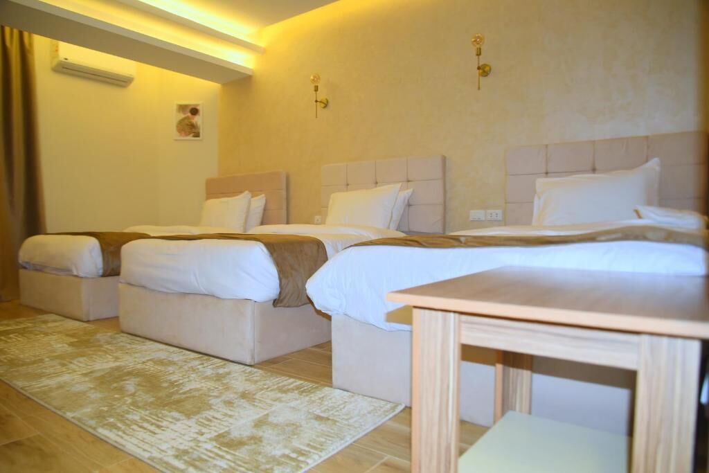 Habitación de hotel con tres camas, una mesita de noche de madera, alfombra color beige y aire acondicionado instalado en la pared.