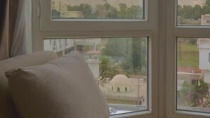 A room with a large window, a beige sofa, and a view of a pyramid. - Pyramids Wonders Hotel (Giza)