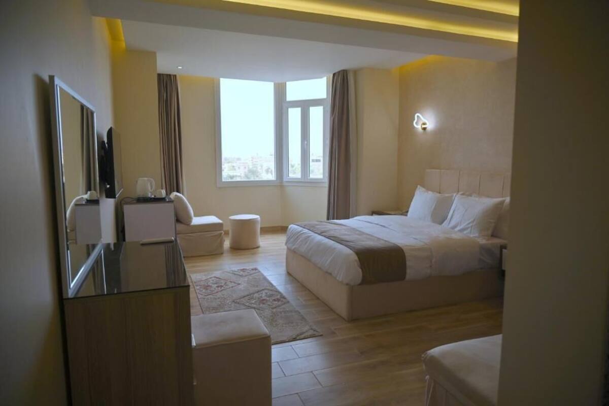 A hotel room with a bed, a desk, a chair, a mirror, a window, and a nightstand.