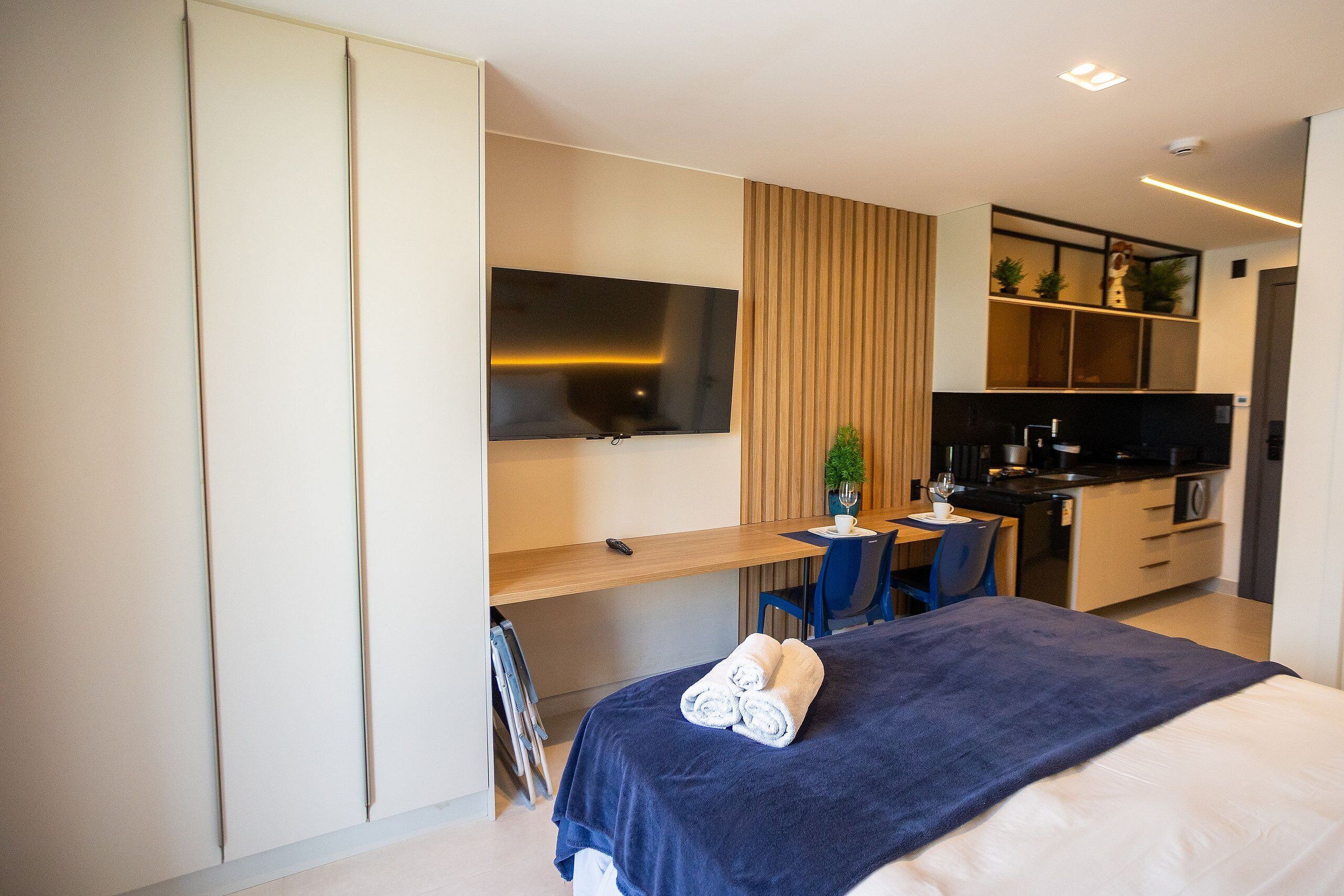 Una habitación de hotel moderna con cama, escritorio, televisor, kitchenette y una silla.