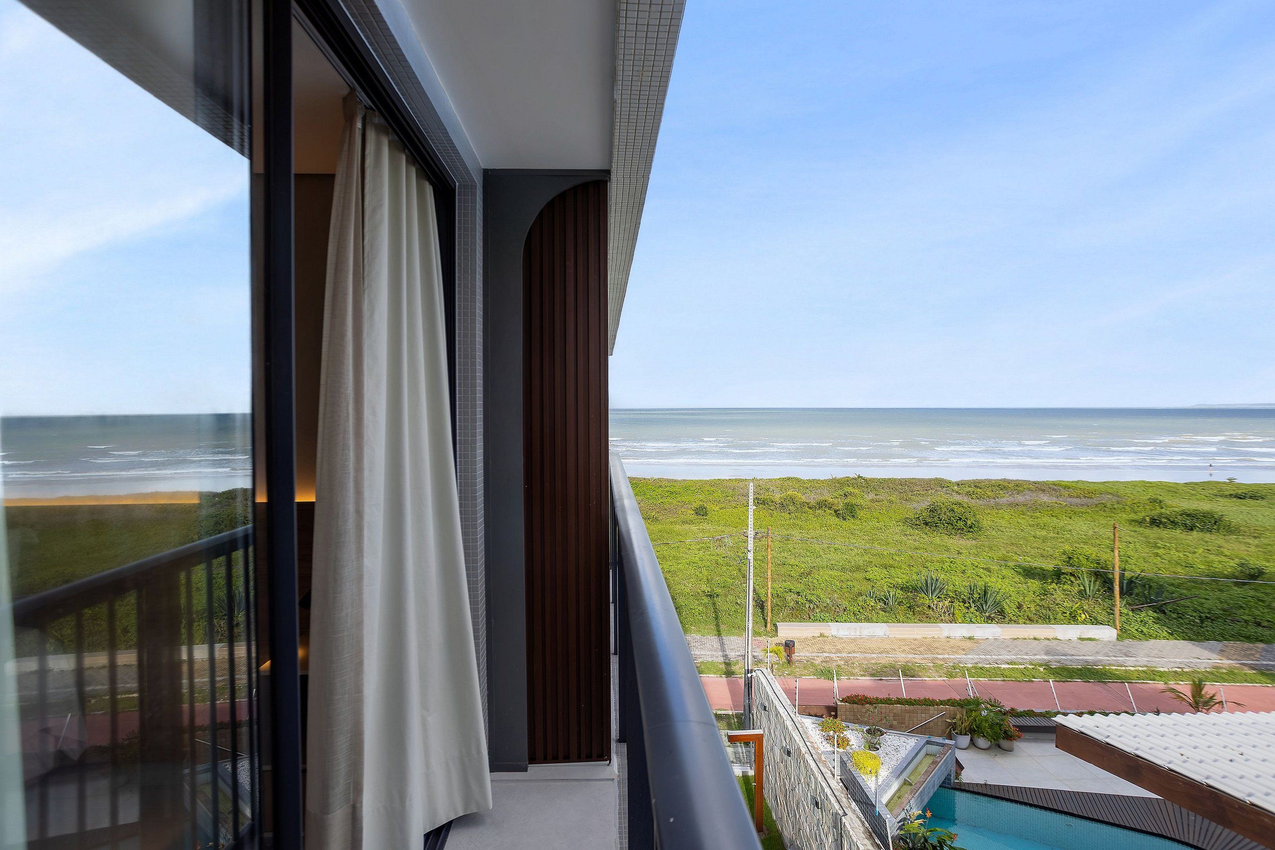 Uma varanda com vista para o oceano, uma piscina e uma área gramada.