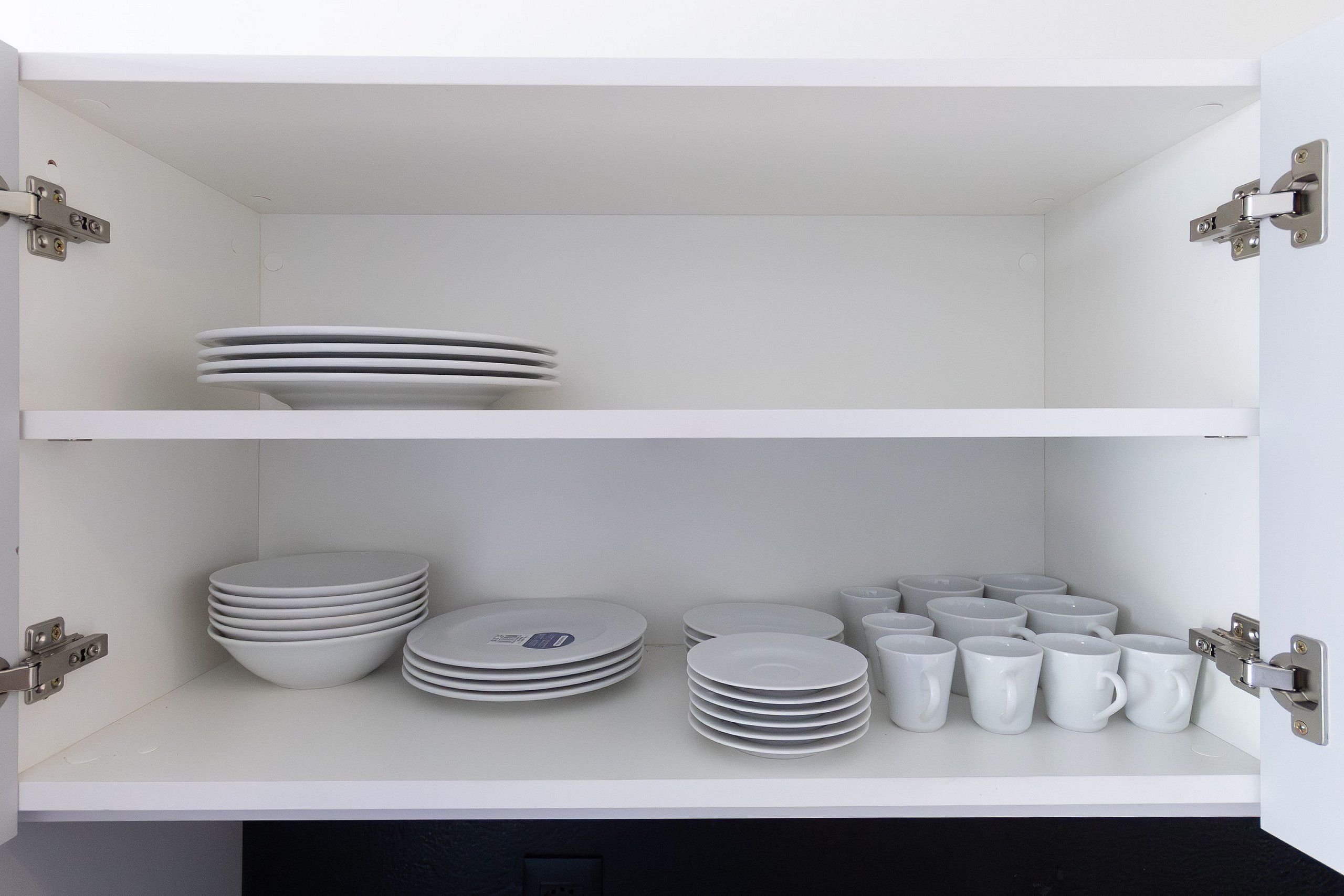 Un mueble blanco con dos estantes, cada uno con pilas de platos y tazas blancos.