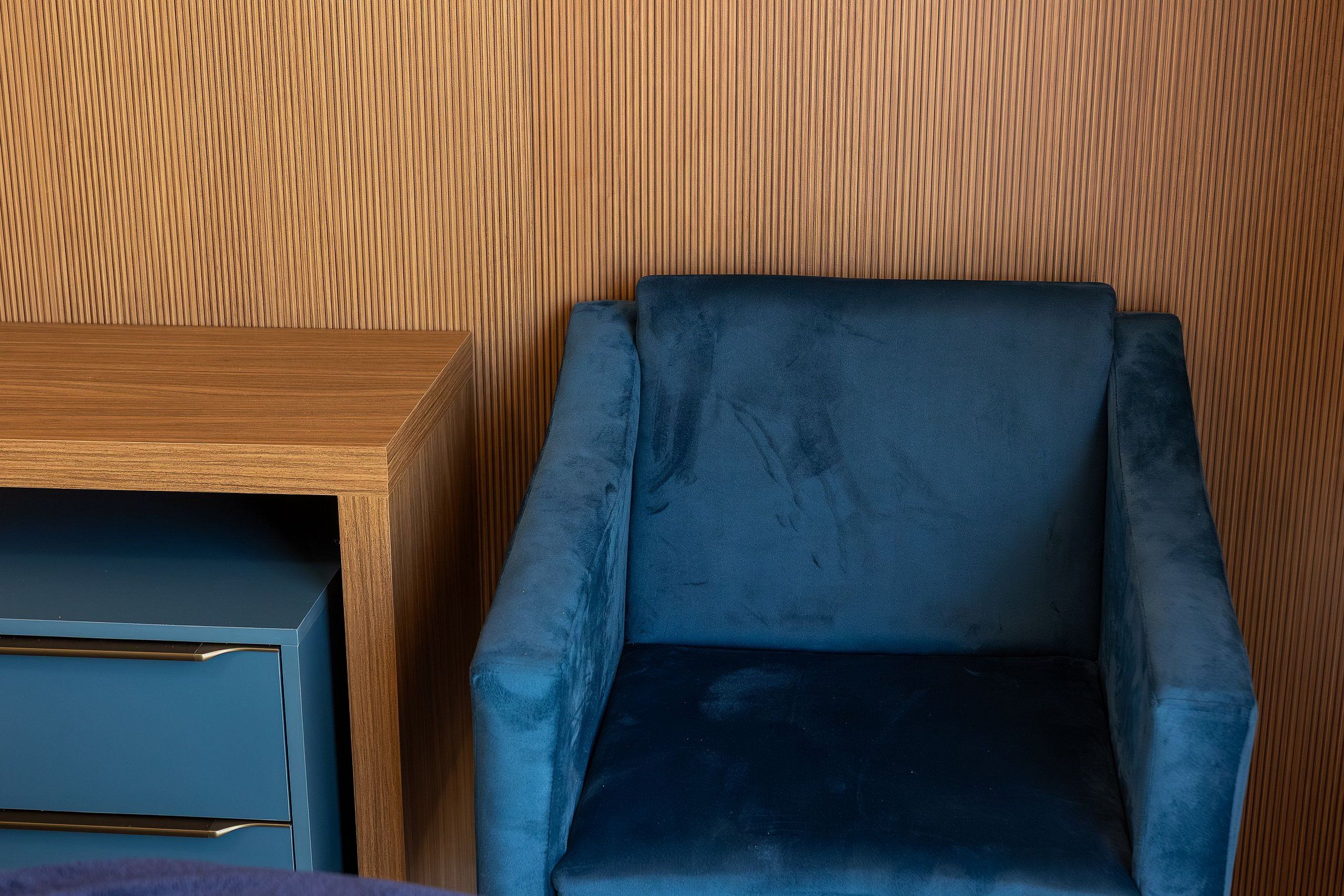 Una habitación con pared de paneles de madera, un sillón tapizado en azul oscuro y una mesita de madera con un objeto de color oscuro encima.
