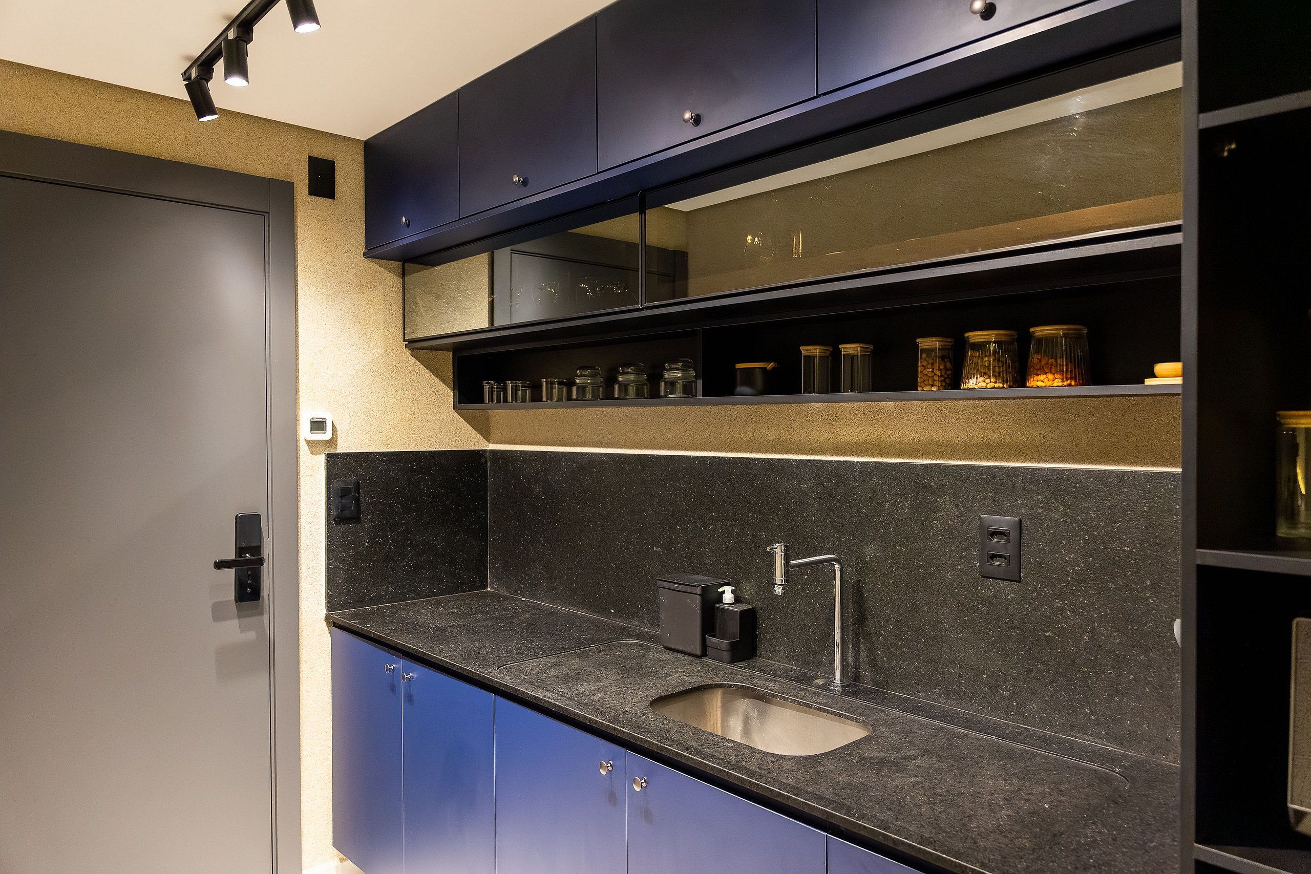 A modern kitchen with a black countertop, stainless steel sink, and a built-in oven.