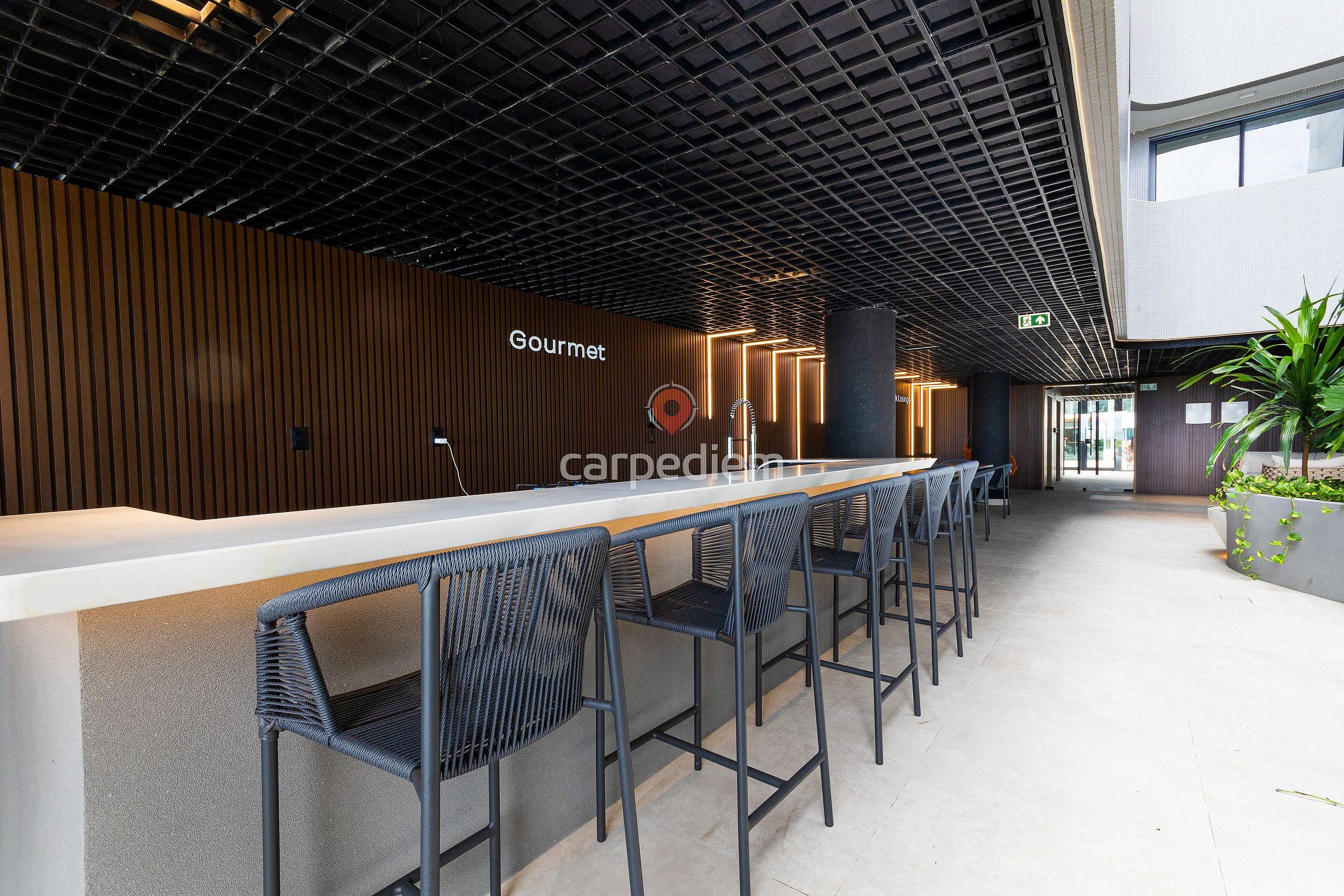 A modern bar area with a long counter, black bar stools, and a sign that reads 'Gourmet.'