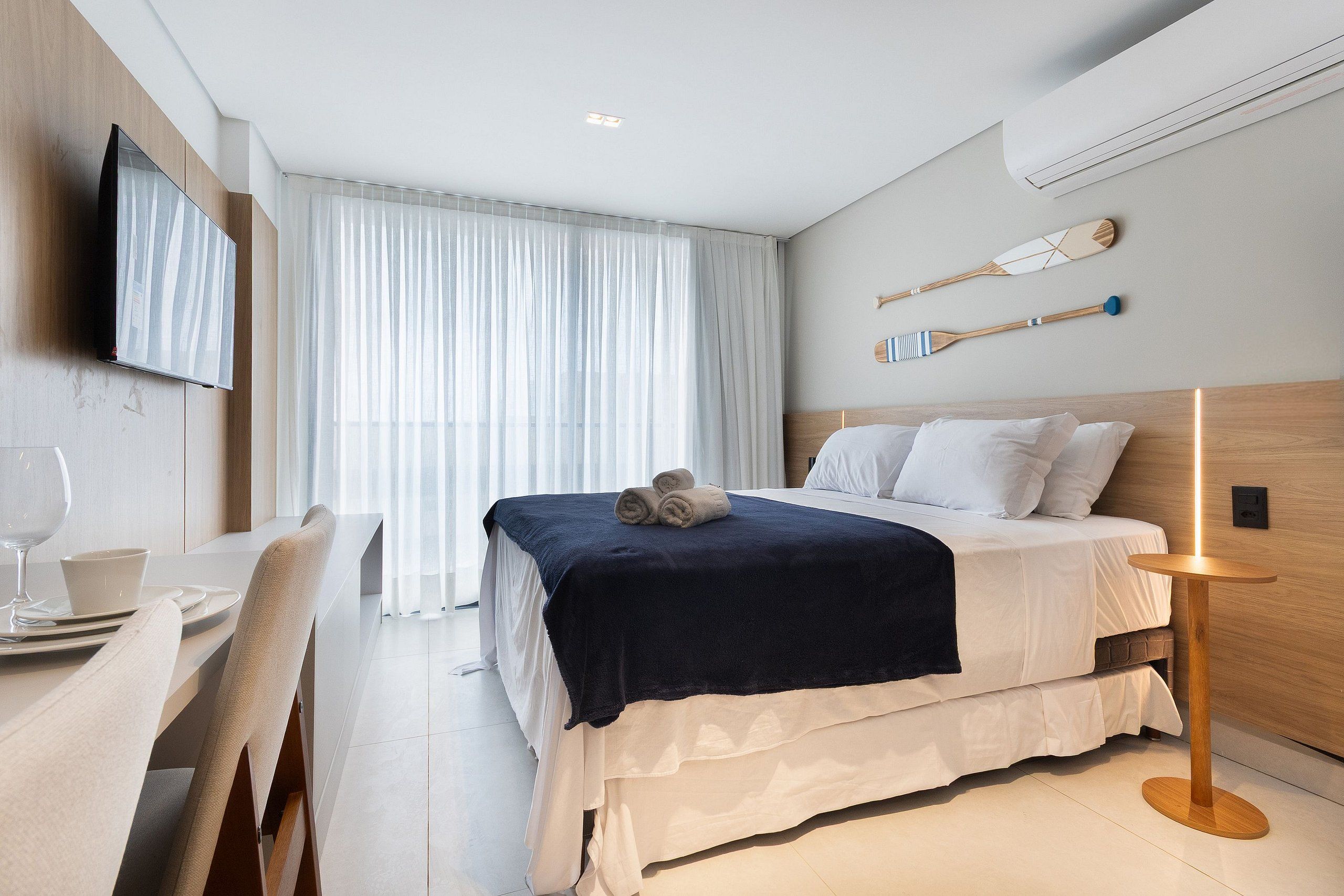 Una habitación de hotel moderna con cama, televisión, zona de comedor y vistas al exterior.
